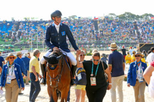 Peder på hästen med många personer runt om och publiken i bakgrunden vid OS